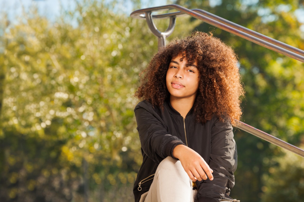 Close-up portrait of beautiful curly African teenage girl sitting at the park in autumn